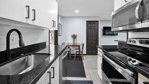 Een moderne keuken met roestvrijstalen apparatuur, een zwart aanrecht en een eethoek met een tafel en stoelen.