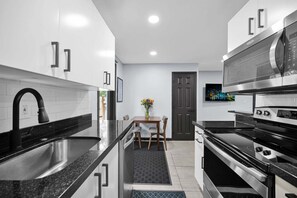 A modern kitchen with stainless steel appliances, a black countertop, and a dining area with a table and chairs. - Bright Designer Villa near Fort Lauderdale / Beach (Wilton Manors)
