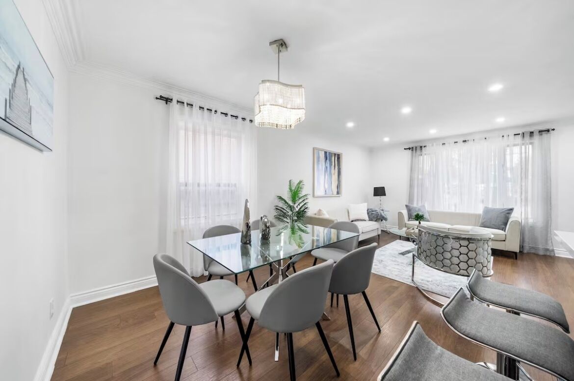 A modern living room with a glass dining table, grey chairs, a sofa, and a patterned coffee table.