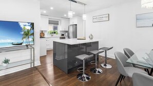 Una cucina moderna con isola centrale, sgabelli da bar, tavolo da pranzo e TV su supporto.
