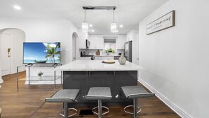 Una cucina moderna con una grande isola, sgabelli da bar, illuminazione a sospensione e una televisione a schermo piatto.