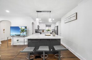 Une cuisine moderne dotée d’un grand îlot central, de tabourets de bar, de luminaires suspendus et d’un téléviseur à écran plat.