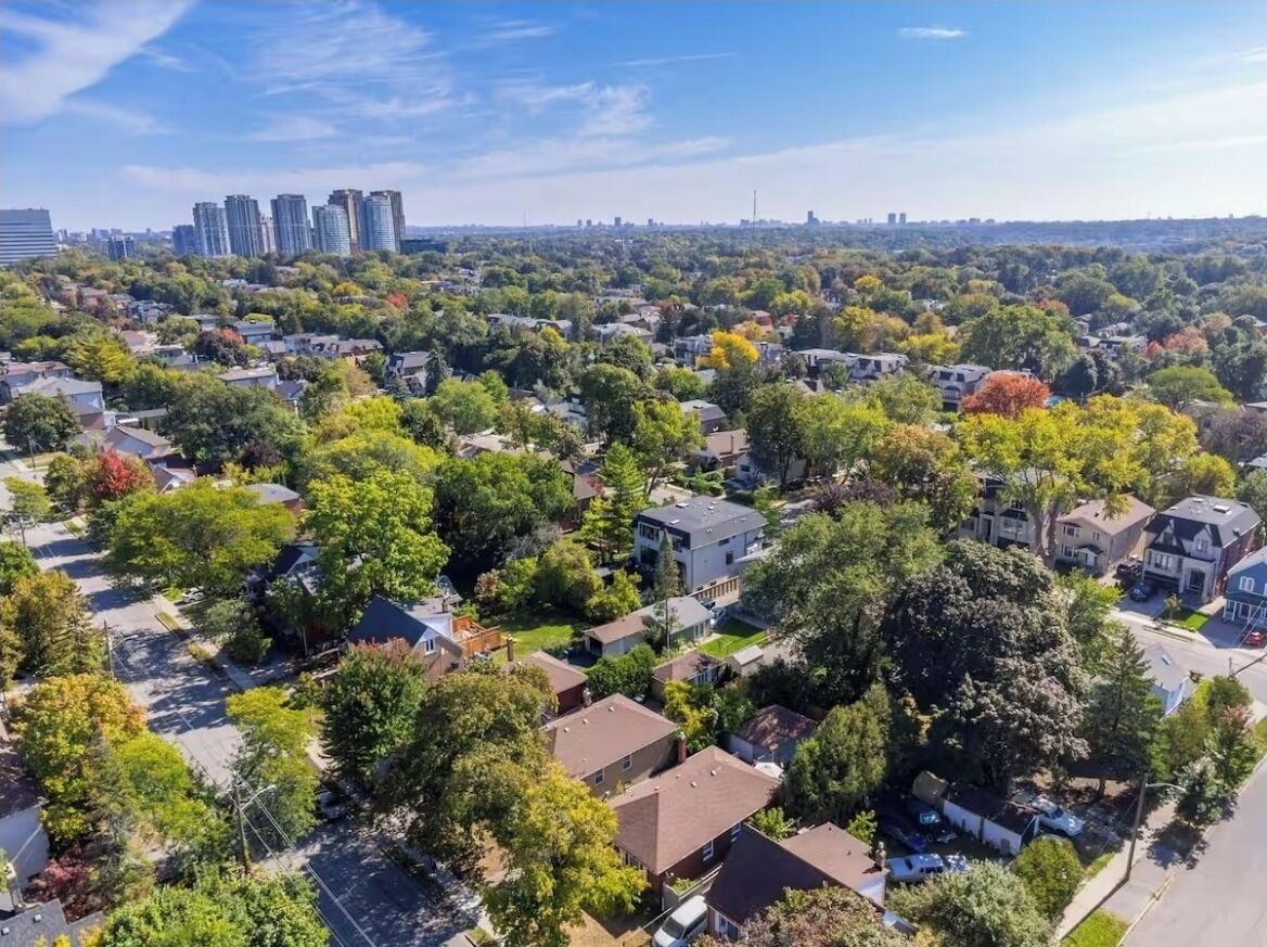 Una vista aerea di una zona residenziale con case, alberi e un profilo urbano lontano.