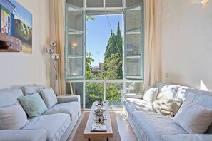 Ein Wohnzimmer mit zwei weißen Sofas, einem Couchtisch mit Dekoration und einem großen Fenster mit Rollläden.
