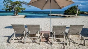 Ein Strand mit drei Korbstühlen und einem großen Sonnenschirm.