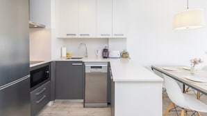 Une cuisine moderne avec des meubles blancs, un lave-vaisselle et un coin repas comprenant une table et des chaises.