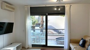 A modern living room with a flat-screen TV, a sofa, a coffee table, and a large sliding glass door leading to an outdoor area. - Sol, terraza y piscina en S’Agaró (Sagaro)