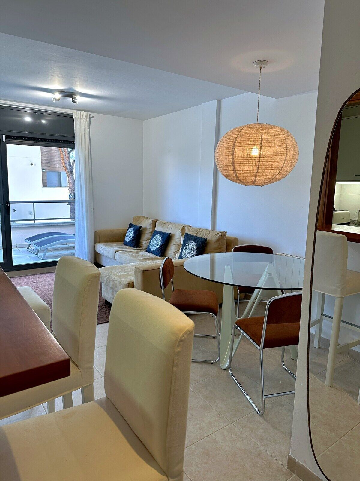 Una sala de estar moderna con un sofá, una mesa de comedor y sillas. Se observa un ventanal con vistas al exterior.
