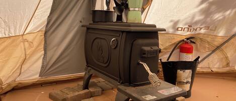 A portable stove with a kettle, a fire extinguisher, and a water bottle on a brick base.