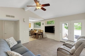 A living room with a ceiling fan, a gray sofa, a dining area with chairs, and a TV mounted on the wall. - Cozy 2-bedroom condo with AC in tranquil St. George (St. George)