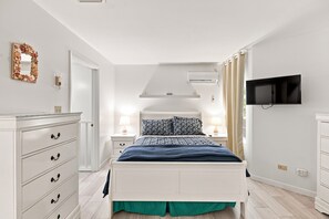 Ein Schlafzimmer mit einem Bett, einem Schminktisch, Nachttischen, einem Fernseher und einer Klimaanlage.