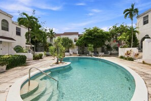 A clear swimming pool surrounded by white buildings with palm trees and a clear blue sky. - 3-bedroom newly renovated condo in tranquil Paradise Island (Paradise Island)
