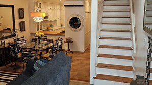 Un salon avec un canapé, un coin repas avec des chaises et une table, une cuisine avec des placards et un escalier.