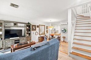 A living room with a TV, wooden furniture, a staircase, and a dining area. - 3-bedroom newly renovated condo in tranquil Paradise Island (Paradise Island)