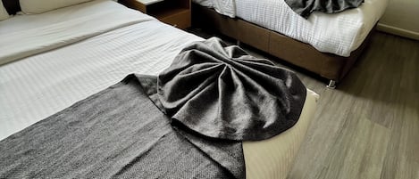 A hotel room with two beds, a bedside table with a lamp, a framed picture on the wall, and a window with sheer curtains.
