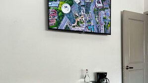 A modern room with a wooden desk, a black Hisense refrigerator, a mounted TV displaying a cityscape, a coffee maker, and a door. - Jazz & Stay (Guadalajara)