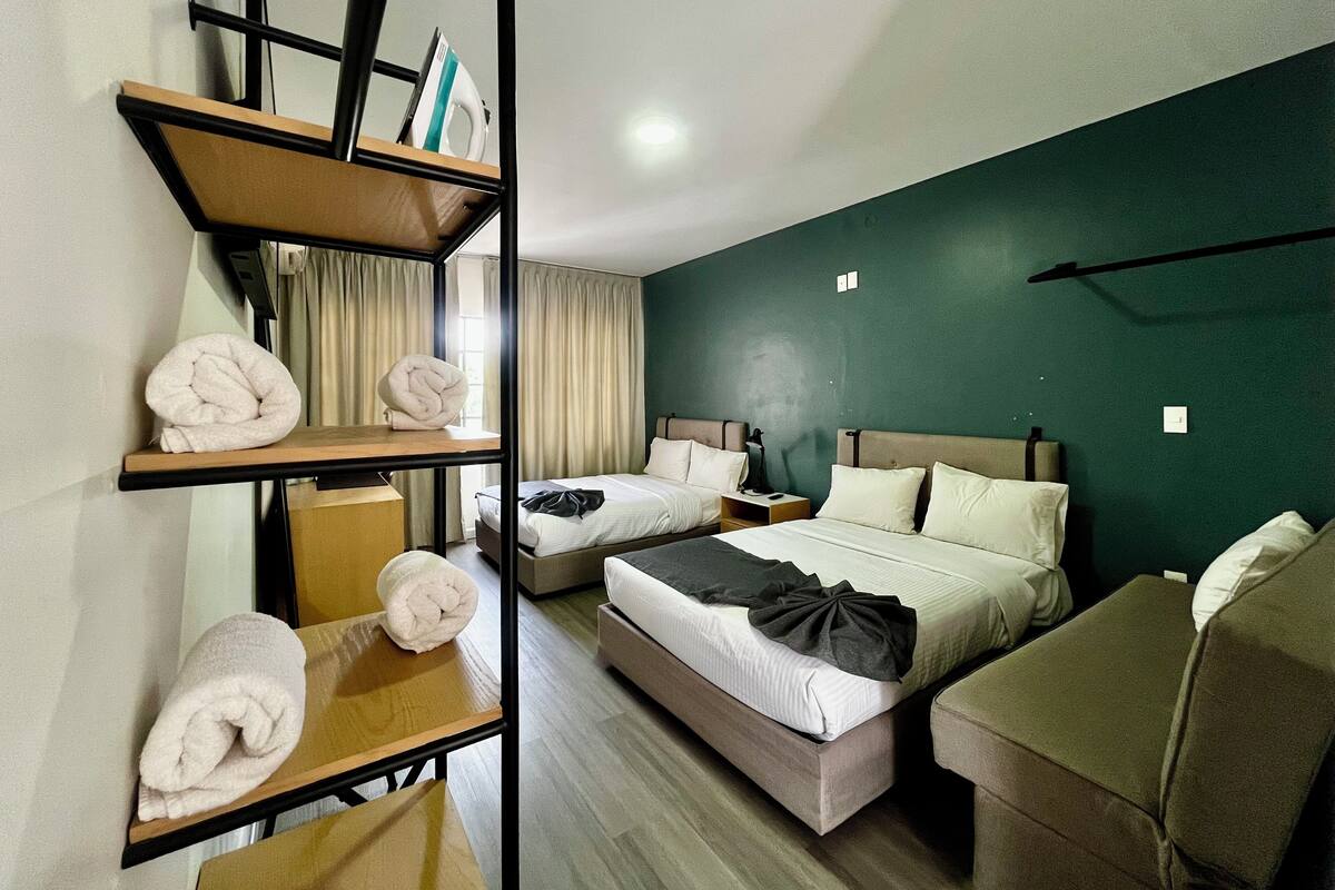 Habitació d'hotel amb una llitera, un escriptori amb mirall, una cadira, dues taules de nit i una paret decorativa verda.