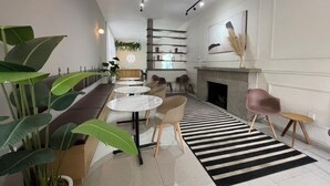 A modern interior with a long bench, round tables, and chairs, a fireplace, and large potted plants. - Jazz & Stay (Guadalajara)
