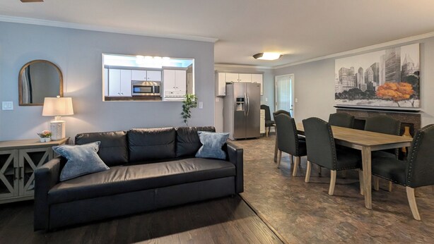 Een woonkamer met een donker leren bank, een eettafel met stoelen, een keuken met inbouwapparatuur, en een stadslandschap schilderij aan de muur.