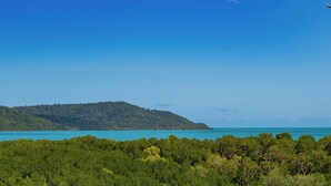 Un paisaje costero con una colina arbolada, cielo despejado y mar tranquilo.