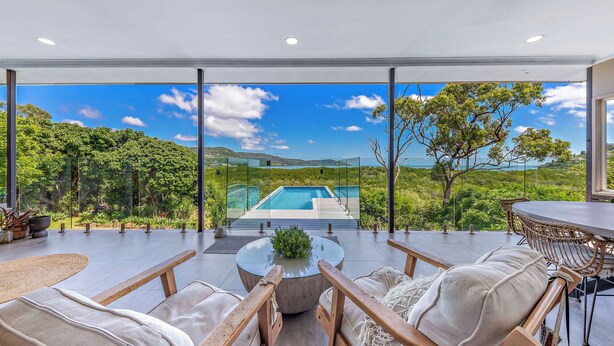 Un espacio moderno con asientos al aire libre, con vistas a una piscina y abundante vegetación.