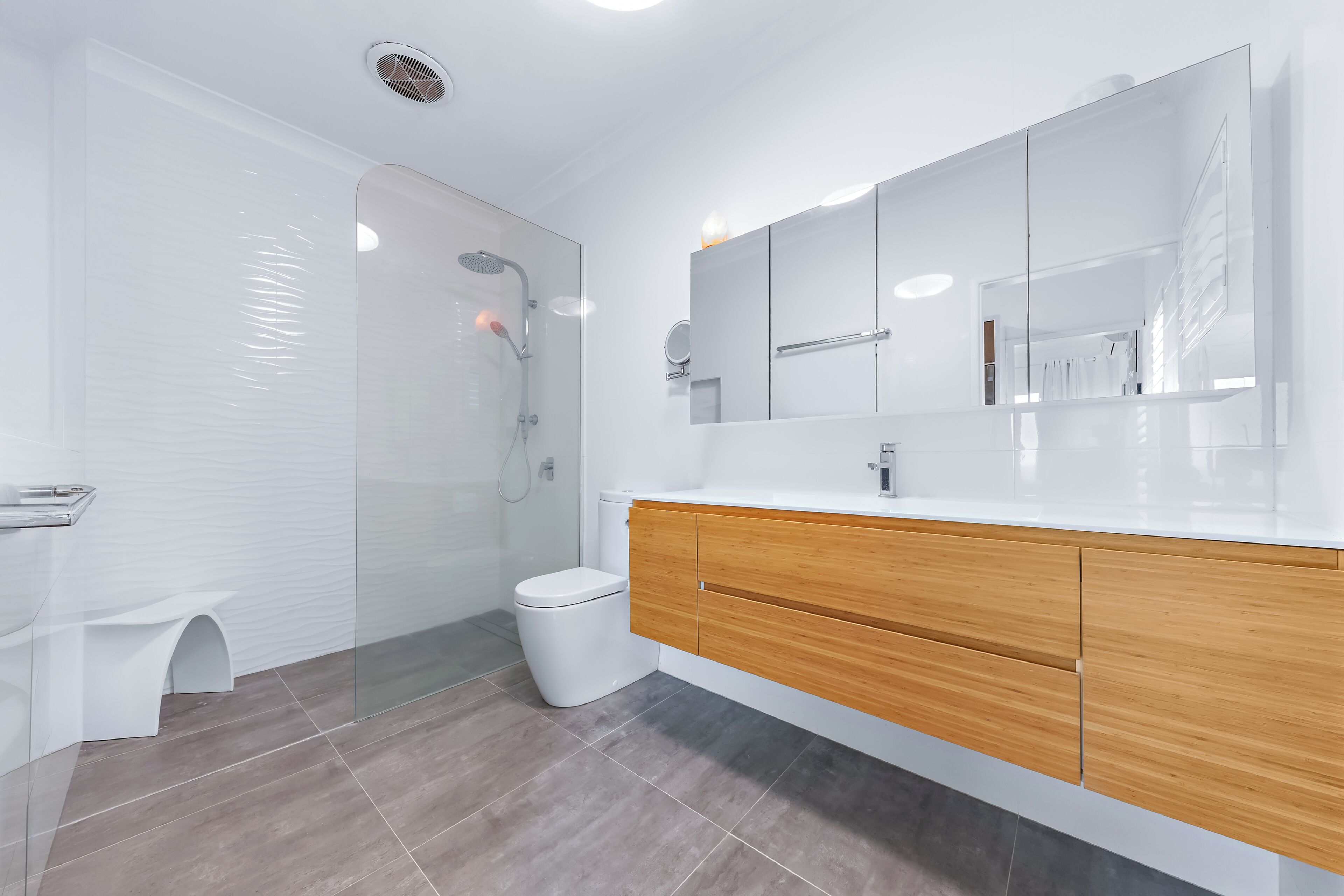Un baño moderno con cabina de ducha de vidrio, inodoro blanco y tocador con muebles de madera.