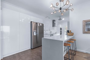 A modern kitchen with stainless steel appliances, a central island with stools, and a decorative chandelier.
