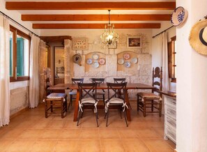 A dining area with a wooden table and chairs, a chandelier, and stone walls. - Charming country house with private pool near Muro (MURO)