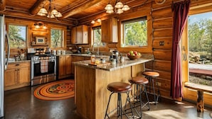 A wooden cabin interior with a kitchen, bar stools, and a view of the outdoors.