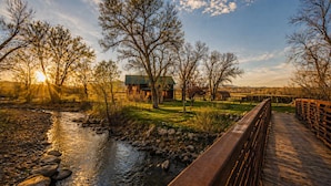 A wooden bridge over a stream with a rustic building in the background.