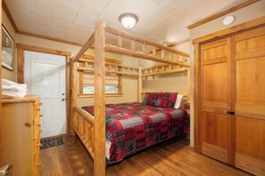 A wooden four-poster bed with a checkered bedspread, a wooden dresser, a door, and a large wooden wardrobe.