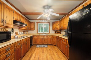 A kitchen with wooden cabinets, a black refrigerator, and a window with a view of trees. - Boulder Retreat | 2BR/2BA Accident w/ Hot Tub (Accident)
