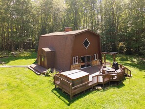 A rustic cabin with a deck and outdoor seating area surrounded by a forest.
