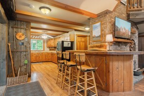 A rustic kitchen with wooden beams, a stone fireplace, and a bar area with stools.