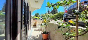 A balcony with a potted plant, a parked car, and a stone wall. - Holiday apartment with terrace (Krk)