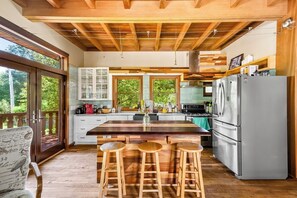 A kitchen with wooden beams, a large island with stools, white cabinets, and a view through the glass door. - Charlestown Retreat | 2 Reflection Pools and Fire Pits (Charlestown)