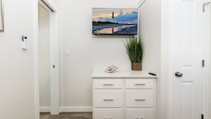 A hallway with a white door, a white dresser with drawers, a potted plant, and a framed picture on the wall. - Near Beach • Pool + Amenities • Sleeps 8 (Middle Township)