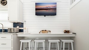 A kitchen with a flat-screen TV, a toaster, a sink, and three white bar stools. - Near Beach • Pool + Amenities • Sleeps 8 (Middle Township)