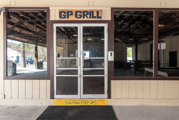 A restaurant entrance with a sign reading 'GP GRILL' and a caution step-up sign at the entrance. - Near Beach • Pool + Amenities • Sleeps 8 (Middle Township)