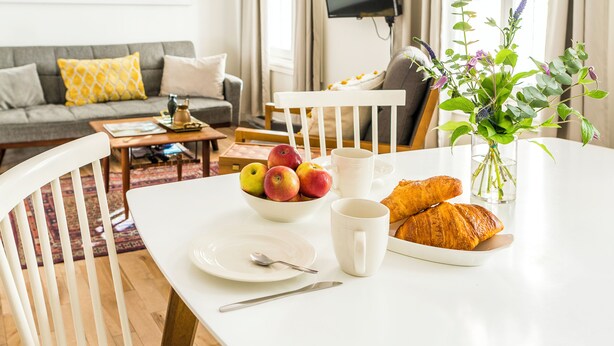Ein Essbereich mit einem Tisch, der für ein Frühstück gedeckt ist, mit Früchten, einem Croissant und einer Tasse.