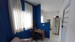 A room with a blue accent wall, a white sofa, a desk with a chair, and a radiator. - Cozy apartment in Interlagos (São Paulo)