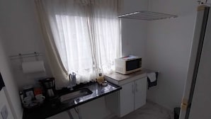 A small kitchen with a sink, a microwave, and a window with curtains. - Cozy apartment in Interlagos (São Paulo)