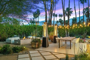 An outdoor patio area with seating, a fire feature, and string lights. - August House - Bold Design, Poolside Fun, Spa, Fire Pit & Views (Palm Springs)