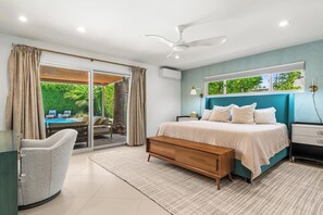 A bedroom with a bed, bedside tables, a bench, a chair, and a view of a swimming pool and greenery. - August House - Bold Design, Poolside Fun, Spa, Fire Pit & Views (Palm Springs)