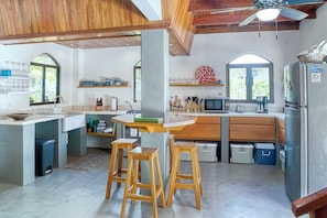 Una cocina con taburetes de madera, un refrigerador, un microondas y un lavamanos.