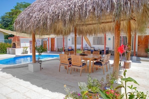 A poolside area with a thatched roof, wooden furniture, and potted plants.