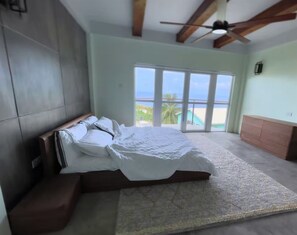 Un dormitorio con cama, ventilador de techo, ventana grande con vistas y cabecera de madera.