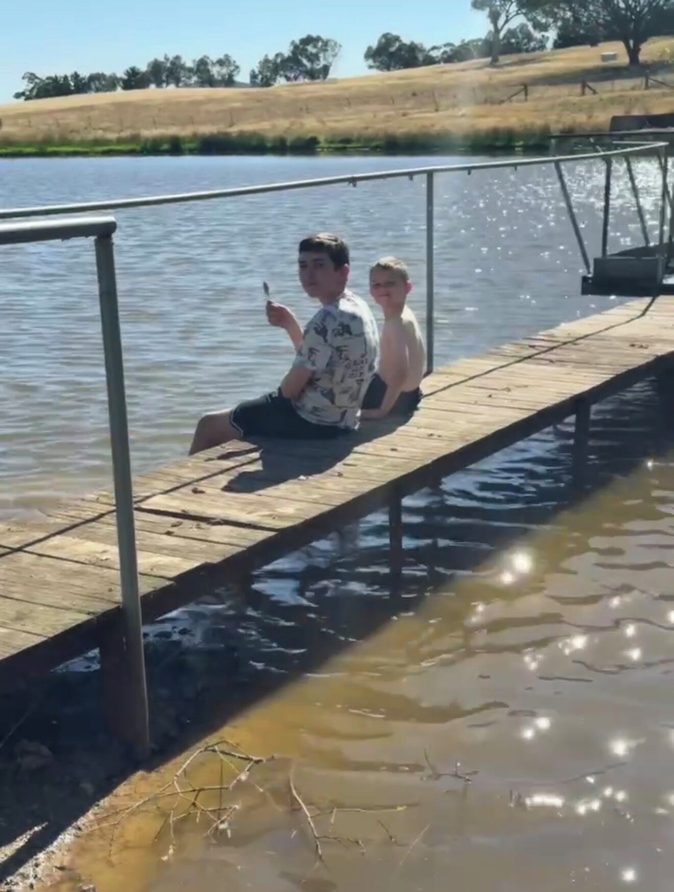 A wooden dock extending over water with a metal railing on one side.