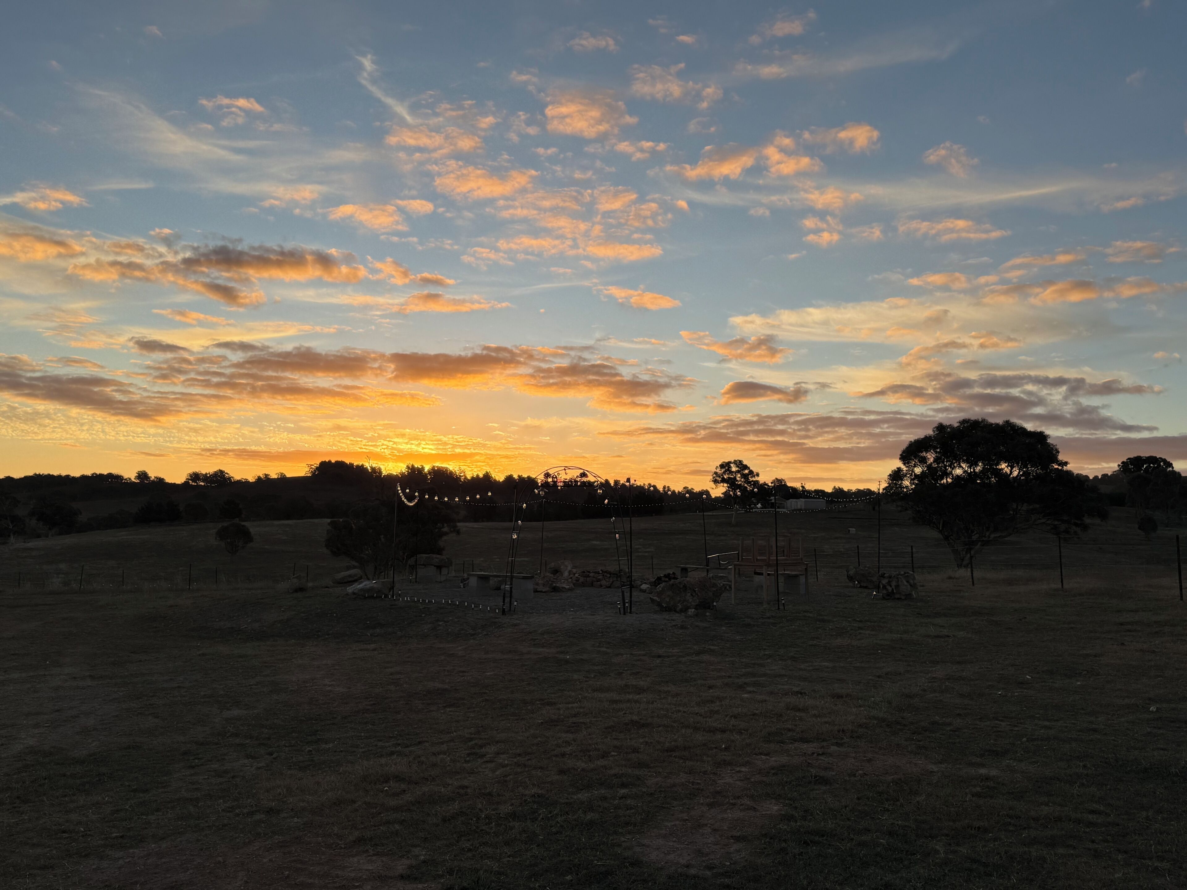Um campo com cerca, árvores e um pôr do sol.