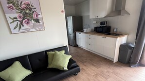 A modern living room with a black sofa, a dining area with a kitchen, and a painting on the wall.